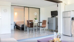 A modern hotel room with a bed, a dining area with a table and chairs, a television, a refrigerator, and a small kitchen area. - Cassis Large studio, Terrace, village and beach on foot, private parking in Provence (Cassis)