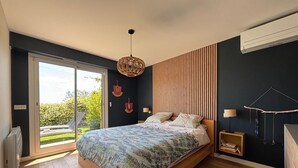 A bedroom with a bed, a wooden floor, a ceiling fan, and a view through a glass door.