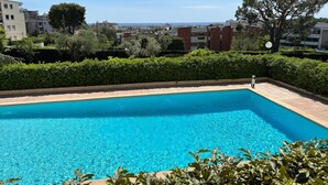 A rectangular swimming pool with clear blue water, surrounded by greenery and buildings in the background.