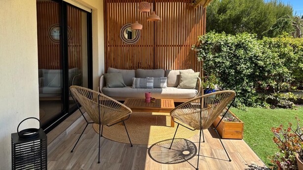 A covered patio with a sofa, two chairs, a small table, and a hanging light fixture.