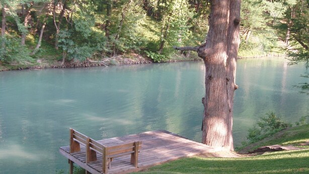 Une jetée en bois s’avançant dans un lac paisible, entourée d’une végétation luxuriante et d’arbres.