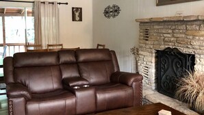 Un salon avec un canapé en cuir marron, une table basse en bois, une cheminée en pierre et un tableau accroché au mur.