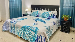 A bedroom with a bed featuring a blue and white coral pattern, a nightstand with a lamp, a potted plant, and a sign on the wall. - Summer and Fall Dates Available! (Cuburna, Progreso)