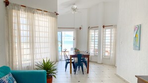 A spacious living area with a teal sofa, a dining table with chairs, and a view of the beach through large windows. - Summer and Fall Dates Available! (Cuburna, Progreso)