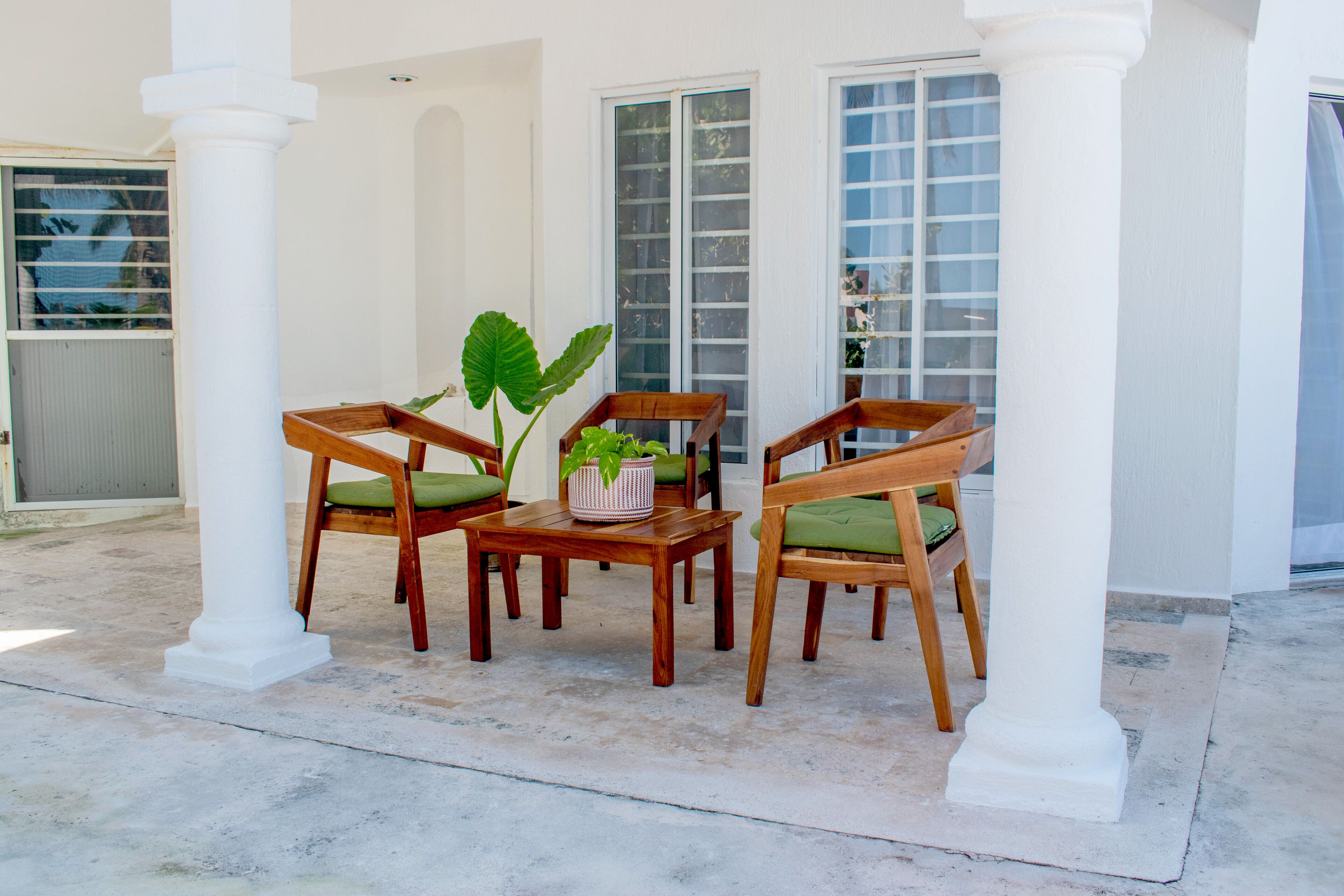 An outdoor seating area with wooden chairs and a table, surrounded by white columns and large windows.