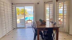 A dining area with a table and chairs, a view of a pool and beach, and a door leading outside. - Summer and Fall Dates Available! (Cuburna, Progreso)