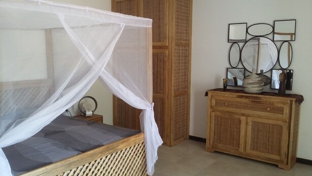 A room with a bed under a canopy, a wooden cabinet with decorative items, and a wall with framed mirrors. - LITTLE PIECE OF HEAVEN (SOMONE)