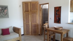A room with a wooden door, a dining table with chairs, a sofa with a red pillow, and a painting on the wall. - LITTLE PIECE OF HEAVEN (SOMONE)