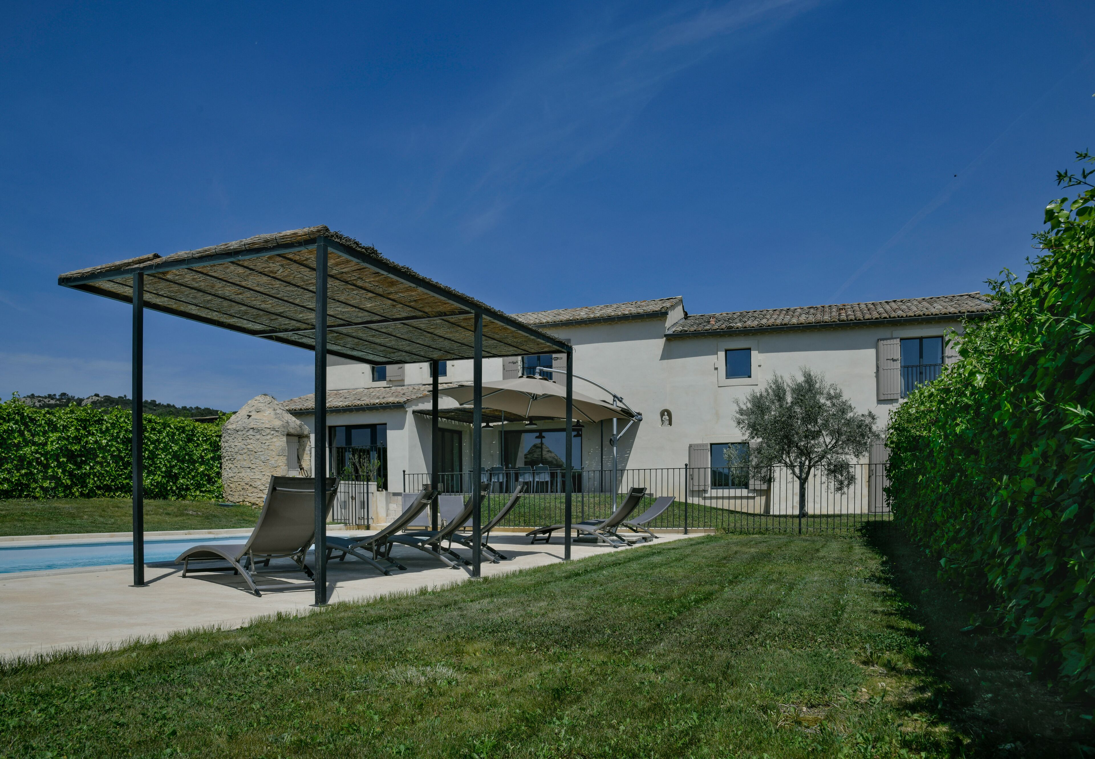 A house with a swimming pool, a covered patio with lounge chairs, and a well-maintained lawn.