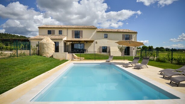 Une maison à deux étages avec une piscine, un espace salon extérieur et un mur en pierre.
