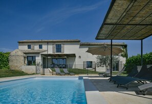 Ein zweigeschossiges Haus mit Schwimmbad, Außenmöbeln und einer überdachten Terrasse.
