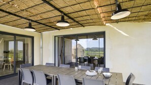 Un espace de restauration en plein air avec une table en bois, des chaises blanches et des lampes suspendues.