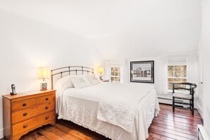 Una camera da letto con un letto, un comodino in legno, due abat-jour, un quadro incorniciato e una finestra con tende.