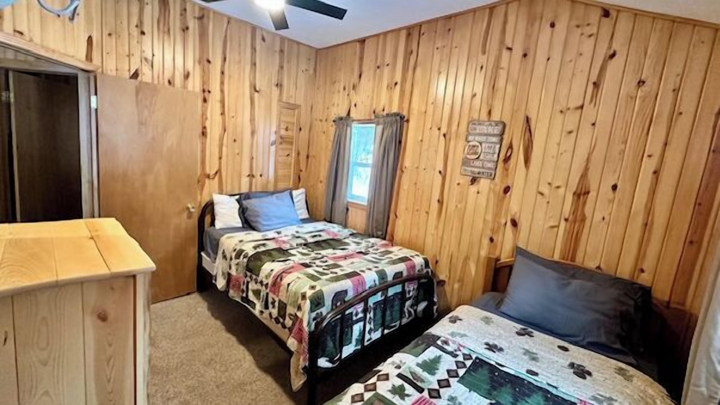Una camera da letto con pareti in legno, un letto con copriletto, un comodino e una finestra con tende.