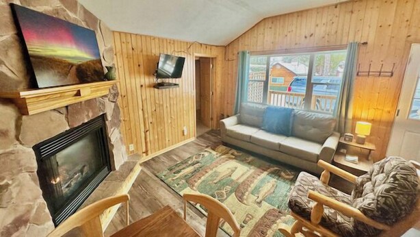Uma sala de estar aconchegante com lareira, televisão, sofá e vista para uma casa pela janela.
