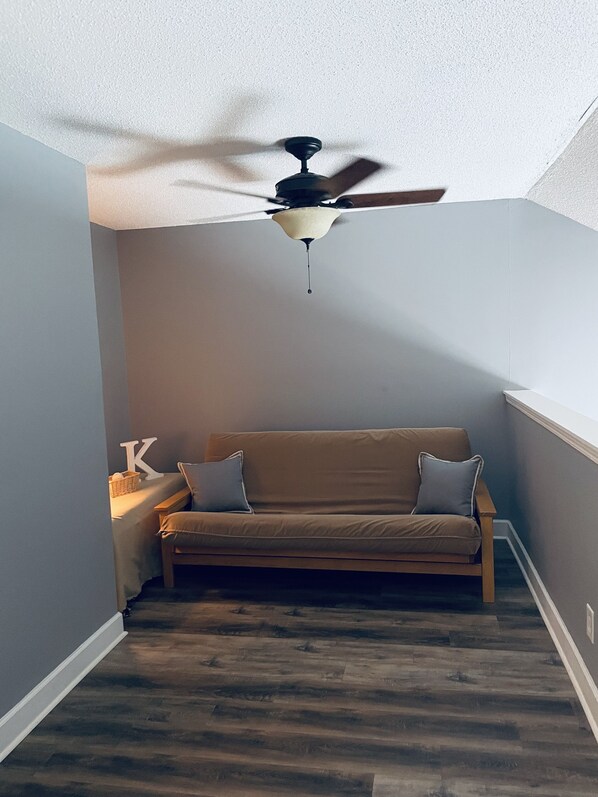 A corner room with a ceiling fan, a brown sofa, and a wooden floor.