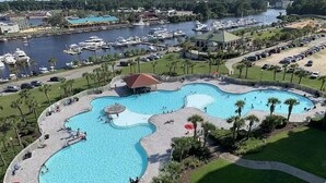 A large, multi-lane swimming pool with a surrounding deck, palm trees, and a marina in the background. - Come spend a few days by  Barefoot Landing available July 10-14 (North Myrtle Beach)