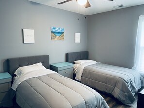 Quarto com duas camas, mesa de cabeceira, ventilador de teto e obra de arte na parede.