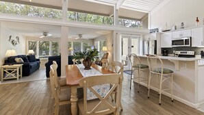 A spacious open-plan living area with a dining table and chairs, a kitchen with modern appliances, and large windows offering views of the outdoors. - SeaPines, Pet friendly, Walk to the Beach Club, Awesome On-site Pool, Updated (hilton head)
