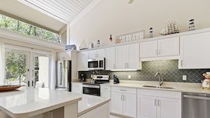 A modern kitchen with white cabinets, a large island, stainless steel appliances, and decorative items on the countertop. - SeaPines, Pet friendly, Walk to the Beach Club, Awesome On-site Pool, Updated (hilton head)