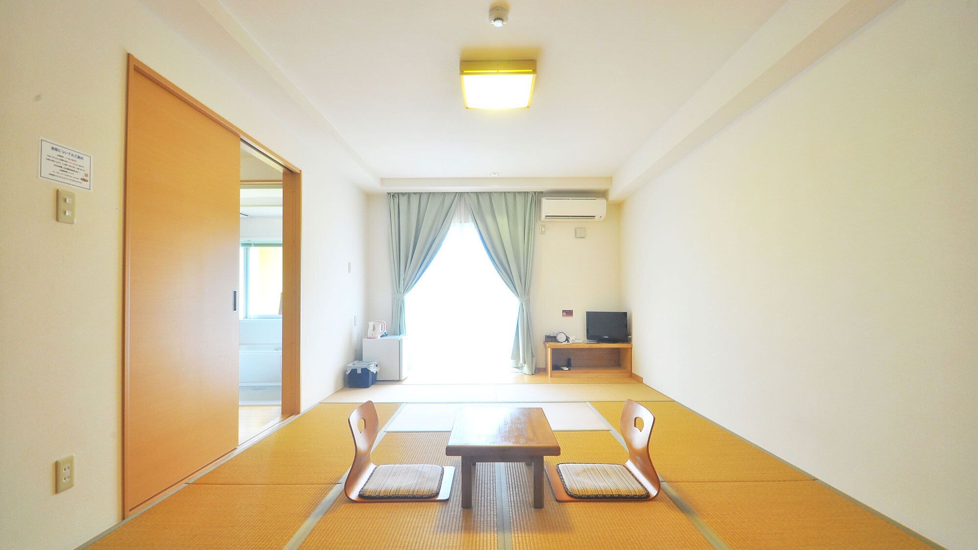 Une pièce avec des tatamis, une petite table, des chaises, un téléviseur et une porte coulissante.