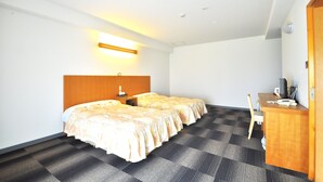 Quarto de hotel com duas camas, uma escrivaninha, uma cadeira e uma luminária.