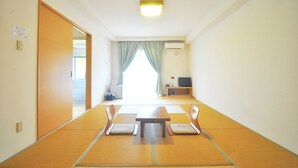 Quarto com esteiras de tatame, uma mesa baixa, duas cadeiras, uma televisão e uma porta deslizante.