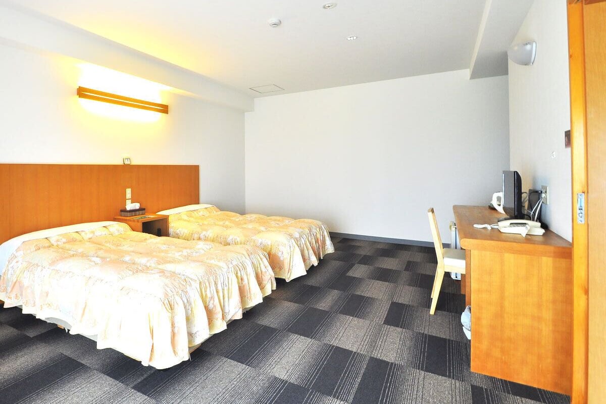 Ein Hotelzimmer mit zwei Betten, einem Schreibtisch, einem Stuhl und einem kleinen Tisch.