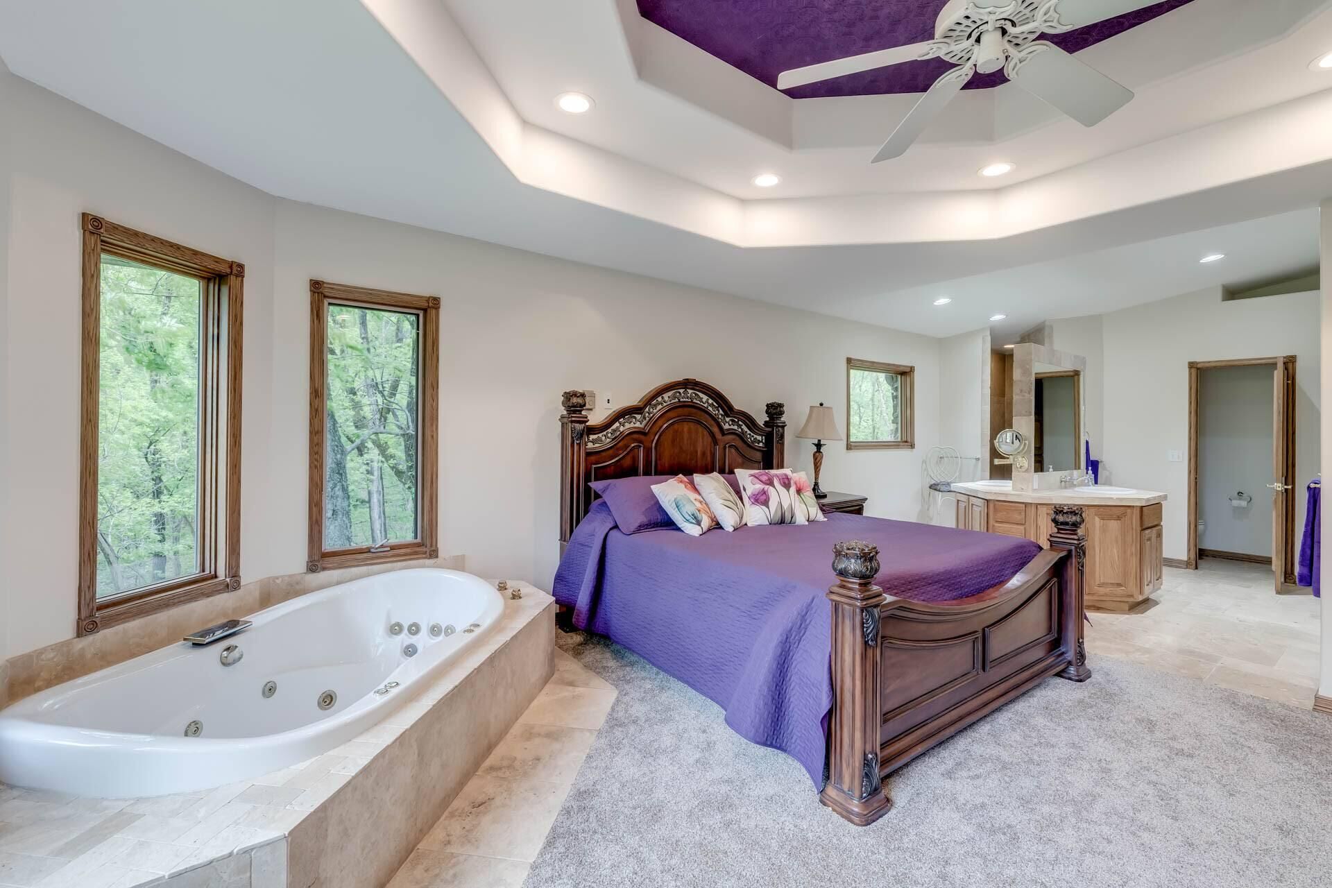 Un dormitorio amplio con una cama grande, baño independiente y vistas a árboles por las ventanas.