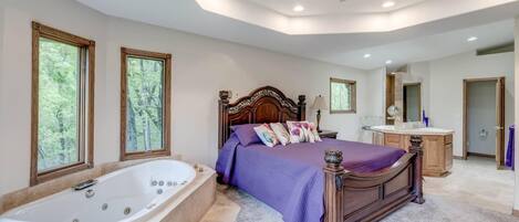 Un dormitorio amplio con una cama grande, baño independiente y vistas a árboles por las ventanas.