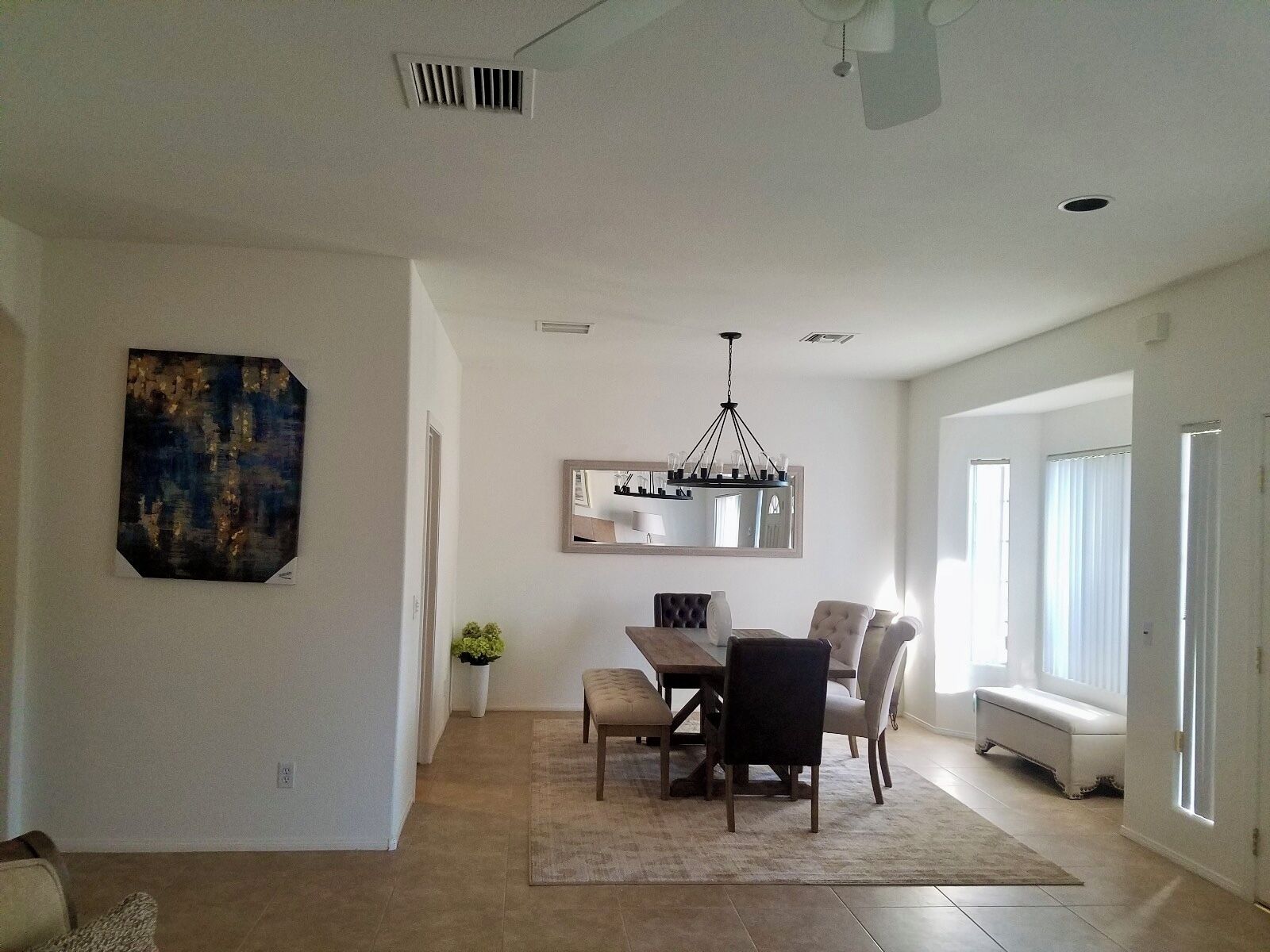 A spacious dining area with a high ceiling, a chandelier, and a large mirror above the table.