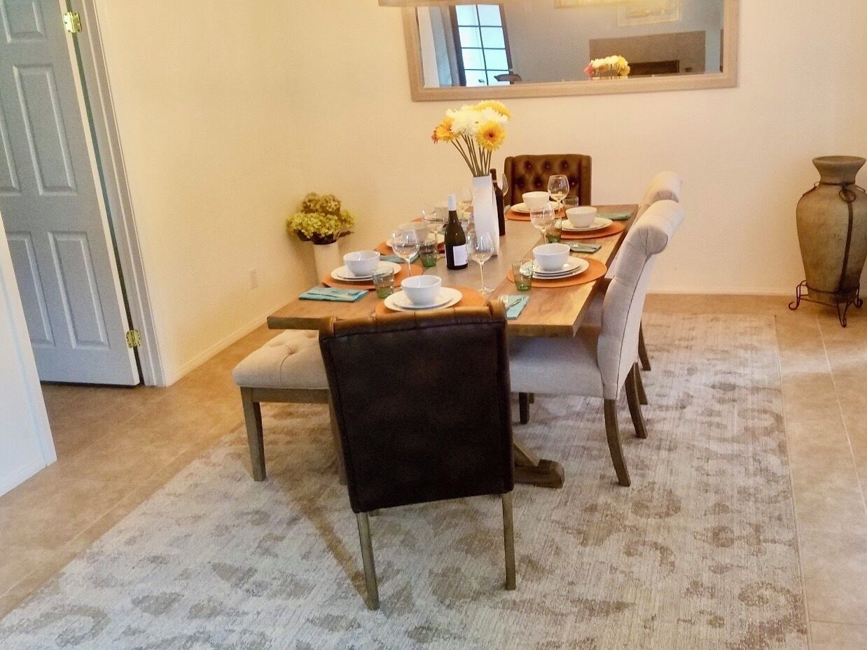 Un coin repas avec une table dressée pour quatre personnes, comprenant des chaises, des assiettes, des verres et un vase avec des fleurs.