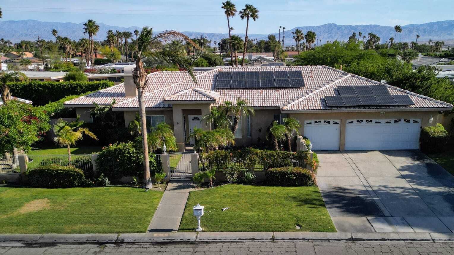 Una casa residencial con techo de tejas, paneles solares, garaje y césped bien cuidado.