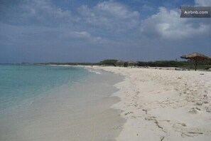 Una playa con aguas turquesas cristalinas, arena blanca y sombrillas de paja.