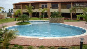 A swimming pool with a brick border, surrounded by grass and palm trees.