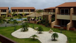 A resort with multiple buildings, a swimming pool, and a landscaped area with palm trees and a thatched-roof structure.