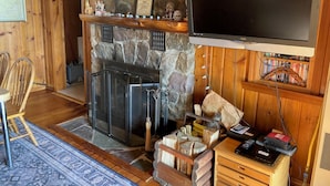 Ein gemütliches Blockhaus-Interieur mit Kamin aus Stein, einem darüber hängenden Fernseher und einem Bücherregal voller Bücher.