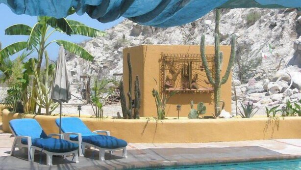Zona de piscina con sillas reclinables azules y un pequeño edificio con ventanal.