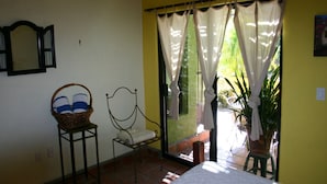 Una habitación con una cama, una silla, una cesta de mimbre y una ventana con cortinas.