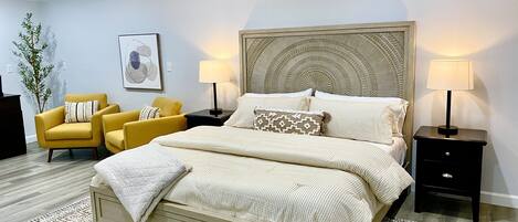 A bedroom with a large bed, two bedside tables, a chair, a floor lamp, and a wall-mounted lamp.