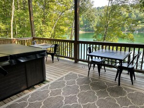 Een overdekt terras met een barbecue en twee tafels, met uitzicht op een meer.