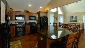A kitchen with wooden cabinets, a black refrigerator, a microwave, and an oven. There is a dining area with a table and chairs. - Rock of Ages-- Huge Dock w/ 2 Covered Slips & Slide; Great House for Holidays! (LaFollette)