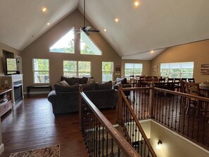 A spacious loft with a high ceiling, large windows, a fireplace, a dining area, and a staircase. - Rock of Ages-- Huge Dock w/ 2 Covered Slips & Slide; Great House for Holidays! (LaFollette)