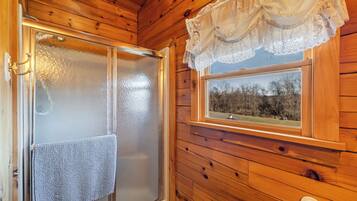 Interior de una cabaña de madera con una puerta de cristal empañado, una ventana con vistas a árboles y un encaje de cortina.