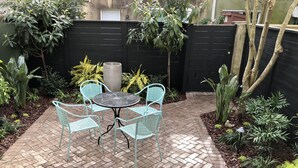 Eine Terrasse mit einem runden Tisch und vier Stühlen, umgeben von Pflanzen und einem schwarzen Zaun.