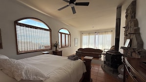 Una camera da letto con un letto, un ventilatore a soffitto, un camino in pietra e ampie finestre.