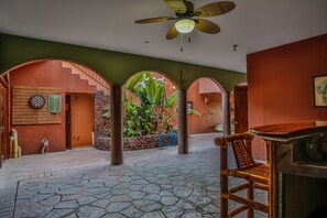 Relax in a spacious area with a high ceiling, ceiling fan, and large archway leading to a serene garden.