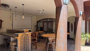 Un ambiente interno accogliente con un'area bar, tavoli e sedie in legno, una grande lavagna e una ventola a soffitto.