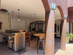 A cozy indoor space with a bar area, wooden tables, and chairs, a large whiteboard, and a ceiling fan.