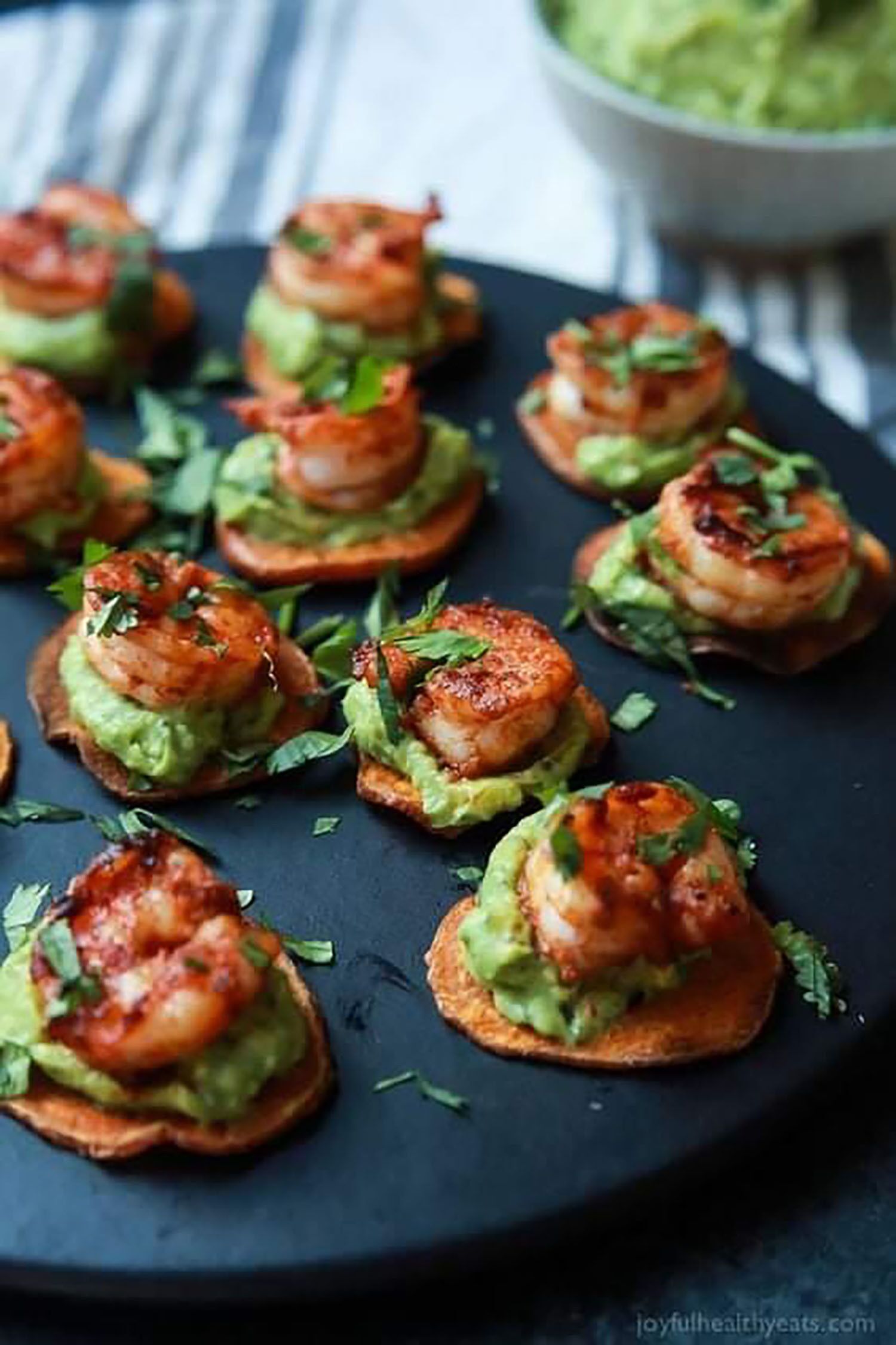 A plate of appetizers with shrimp and avocado on toast, garnished with herbs.